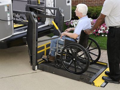 A non-emergency medical transportation representative is loading a wheel chair customer into a medical transportation vehicle.